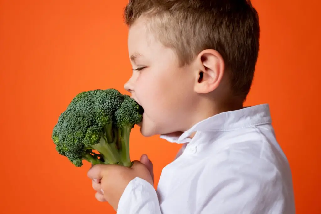 Niño comiendo brócoli en fondo naranja