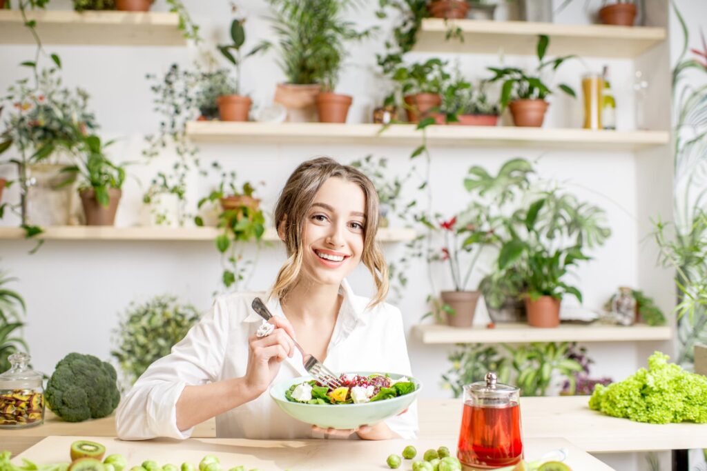 Mujer joven comiendo grasas saludables de origen vegetal y de fondo plantas