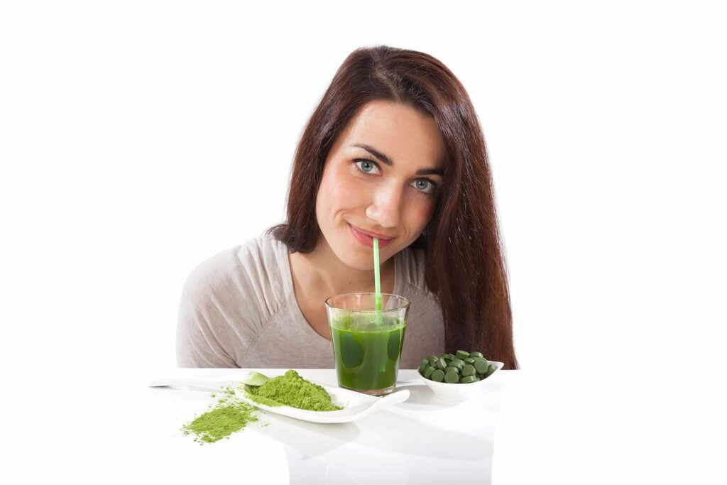 Mujer joven tomando jugo verde con espirulina