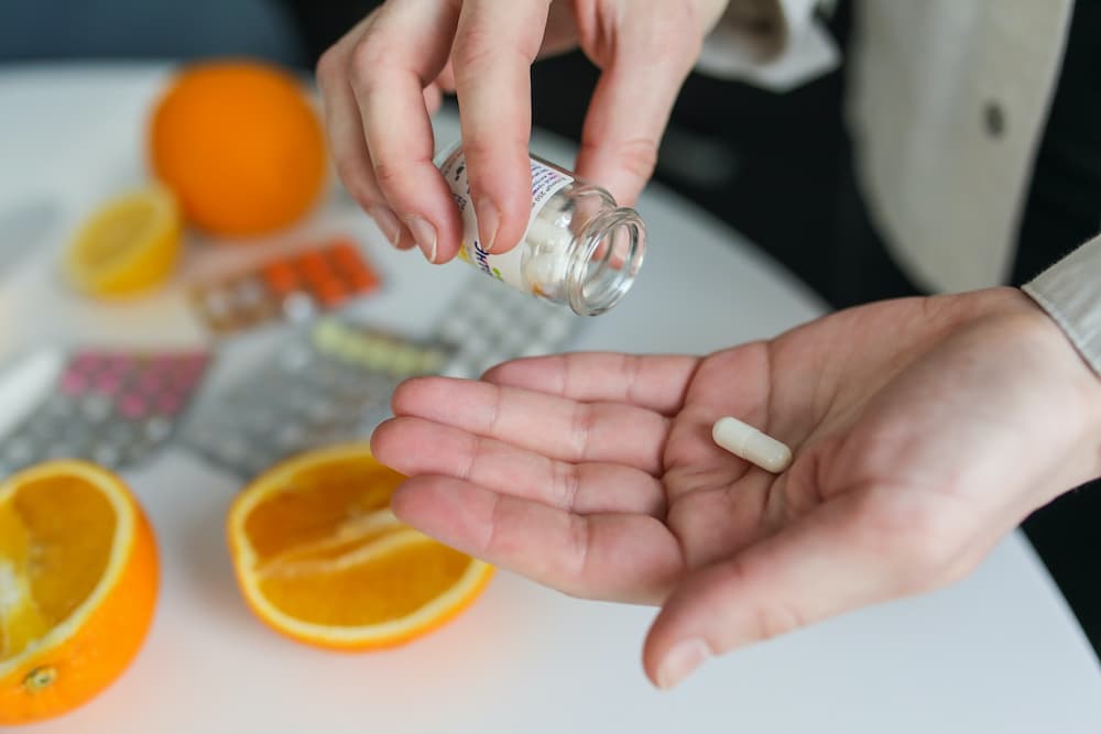 vitamina d mano de mujer con capsula en la mano y naranja